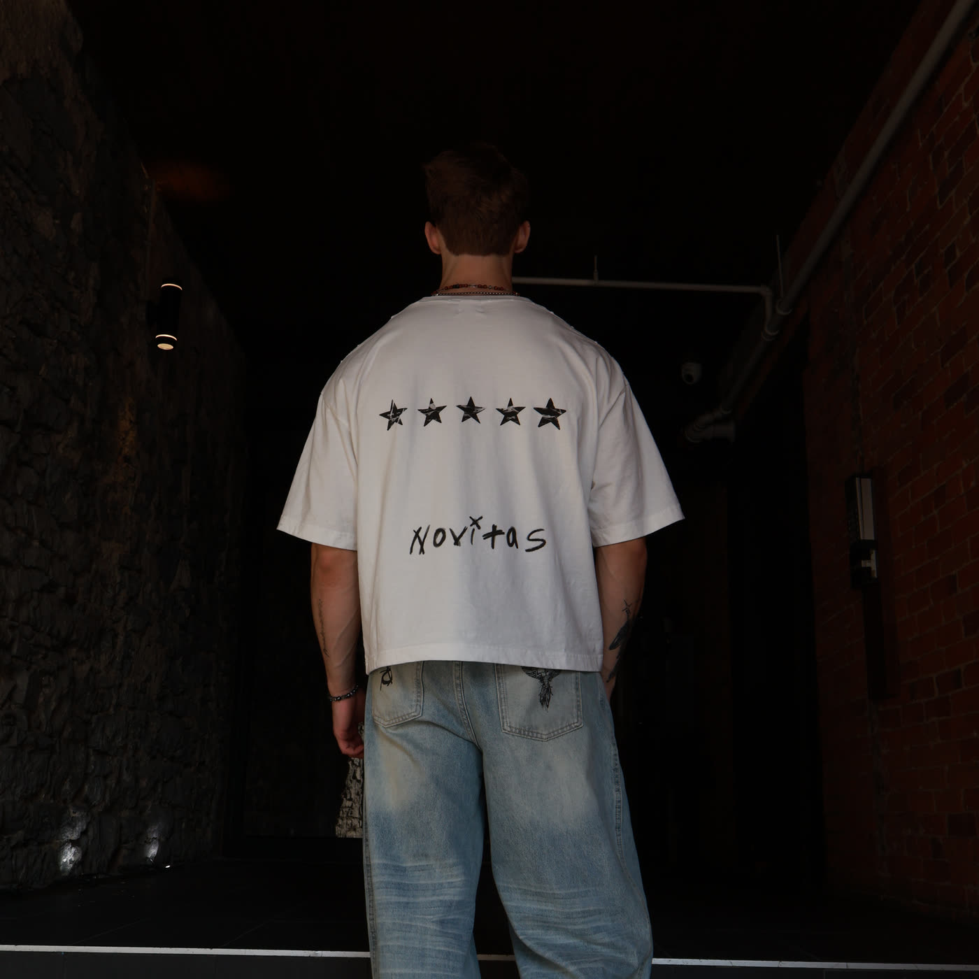 T-shirt Novitas blanc à cinq étoiles, porté de dos dans une ruelle en pierre
